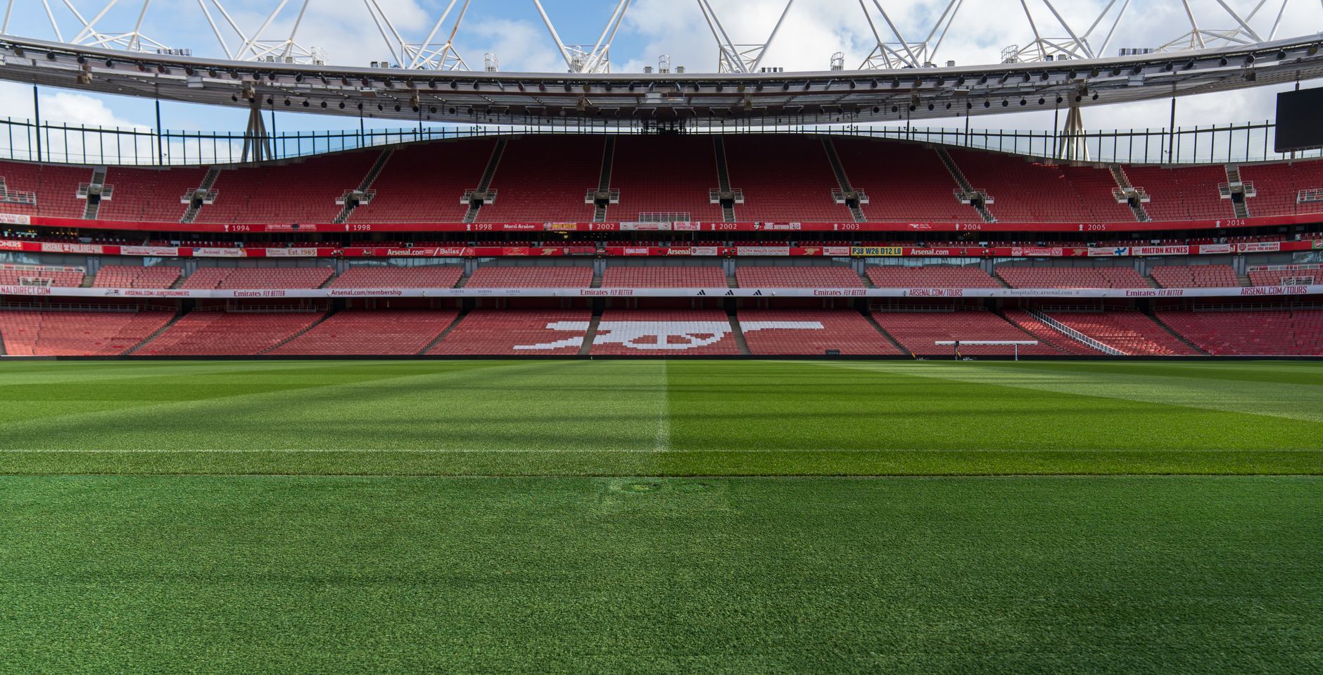 Pelouse verte au premier plan et tribunes rouges d’un grand stade de football.